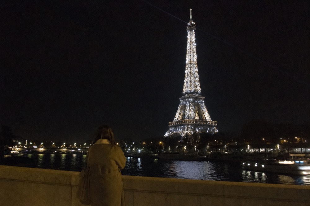The Eiffel Tower mid-sparkle above dark river water, no text, no logos, no people