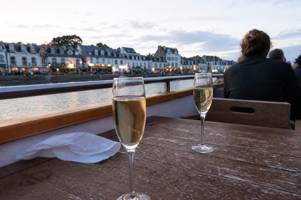 Two champagne flutes on a wooden boat table with Paris rooftops beyond, no text, no logos, no people