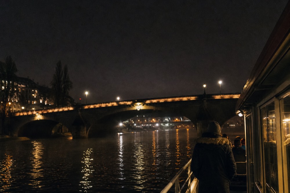 Evening view of the illuminated Seine with a passenger boat's lights reflected on the water, no text, no logos, no people