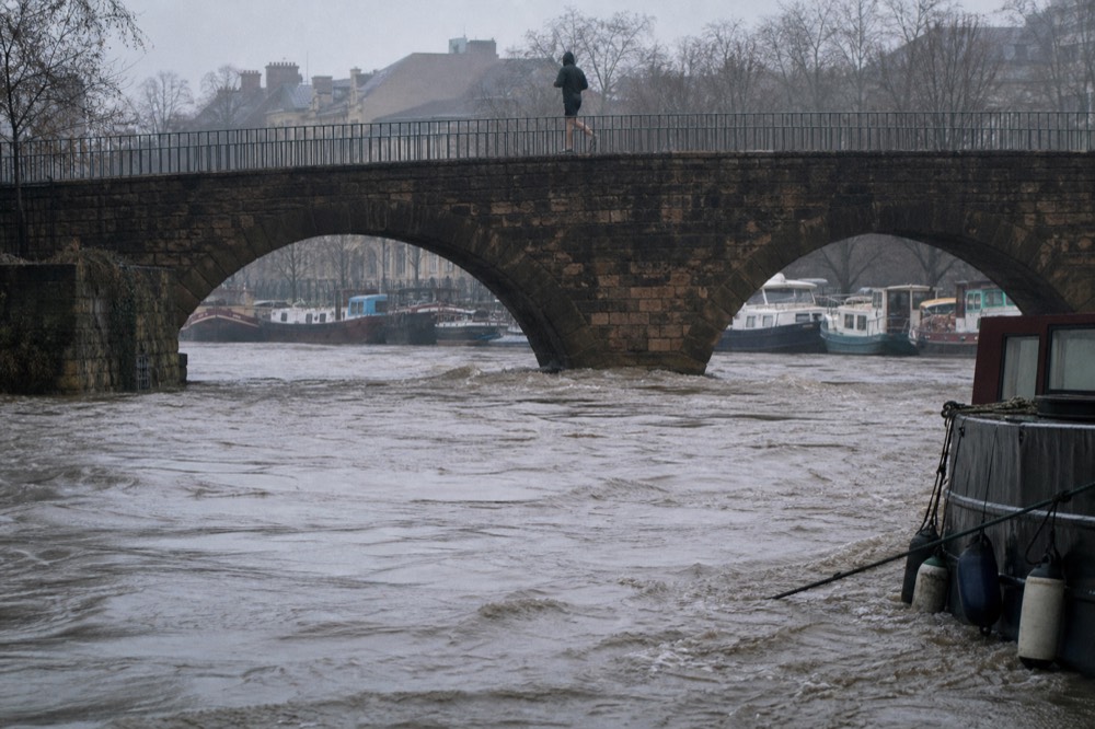 High muddy Seine water under the Pont Neuf with moored boats, no text, no logos, no people
