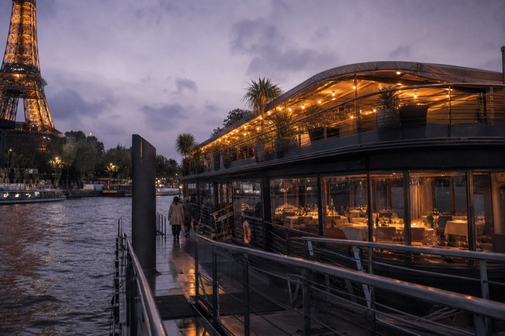 A premium dinner cruise boat with lit terrace on the Seine at dusk, no text, no logos, no people