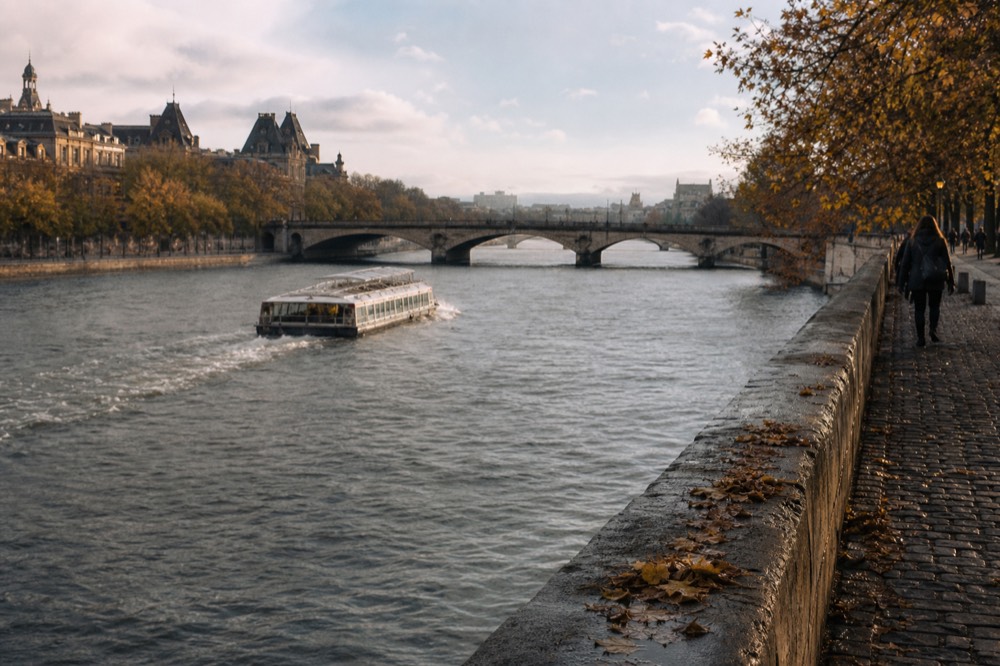 Wide view of the Seine with bridges and a passing boat seen from a quay, no text, no logos, no people.